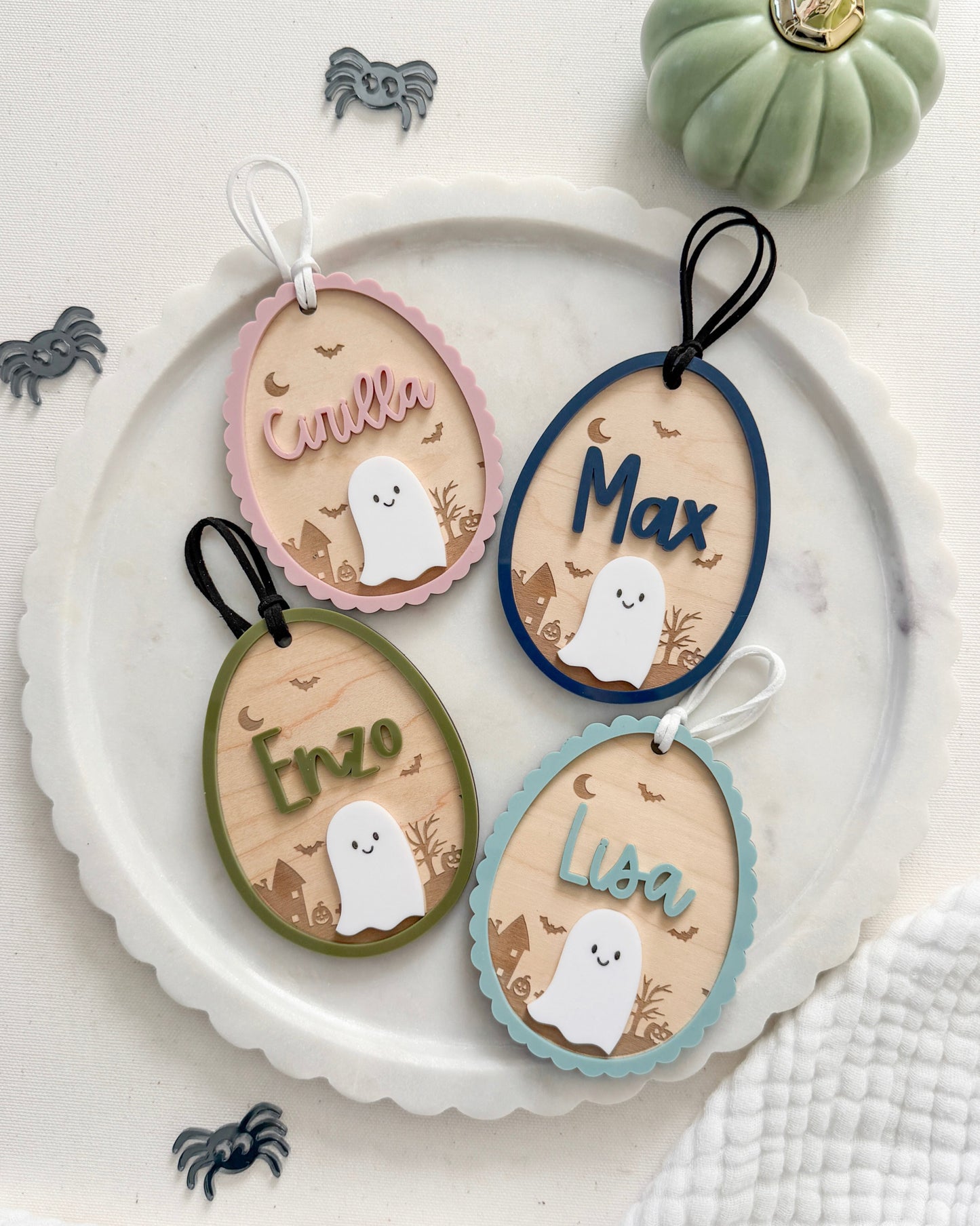Decorative name tags with ghost illustrations on a white plate, surrounded by small pumpkins and spiders.