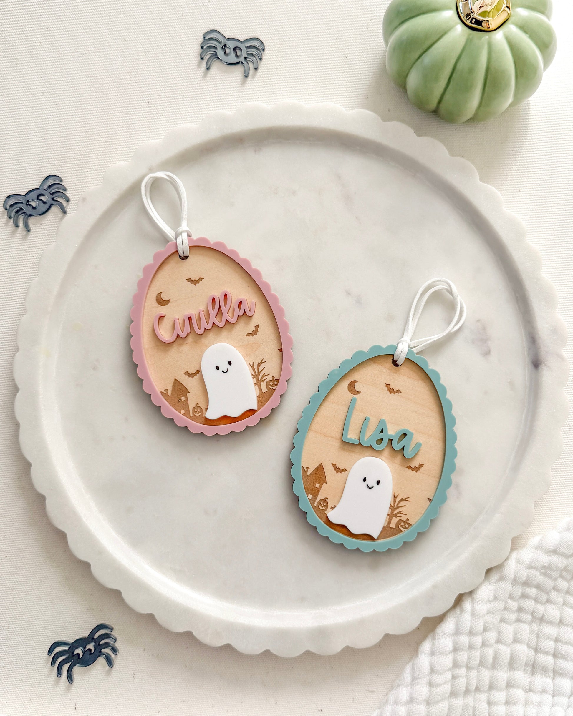 Two oval-shaped ornaments with ghost designs on a white plate, surrounded by small decorative items.
