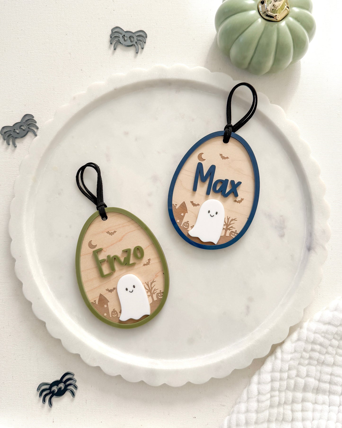 Two oval-shaped Halloween-themed name tags on a white plate with decorative pumpkins and spiders.