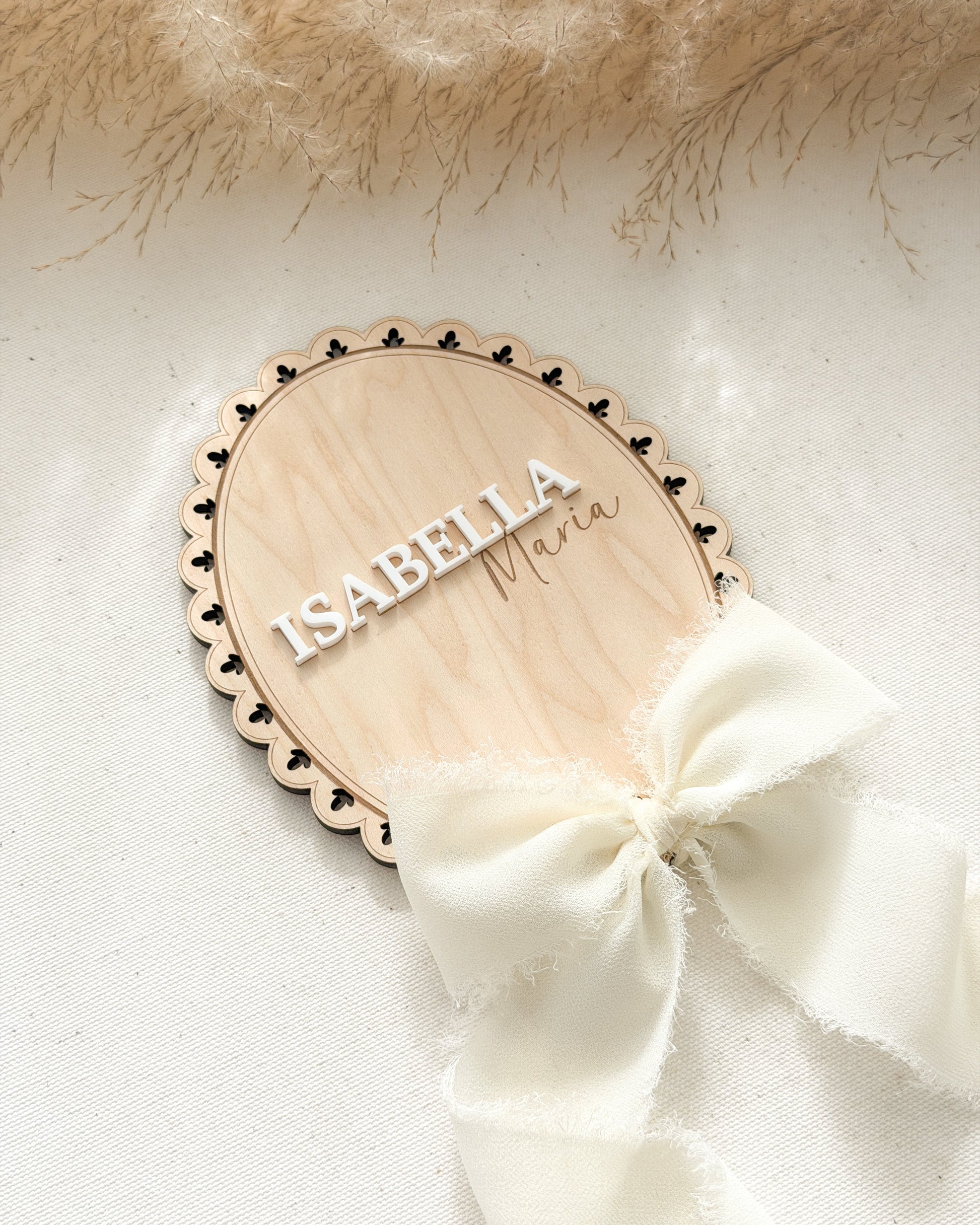 Wooden name plaque with 'Isabella' on a white background with a white bow and beige fur.