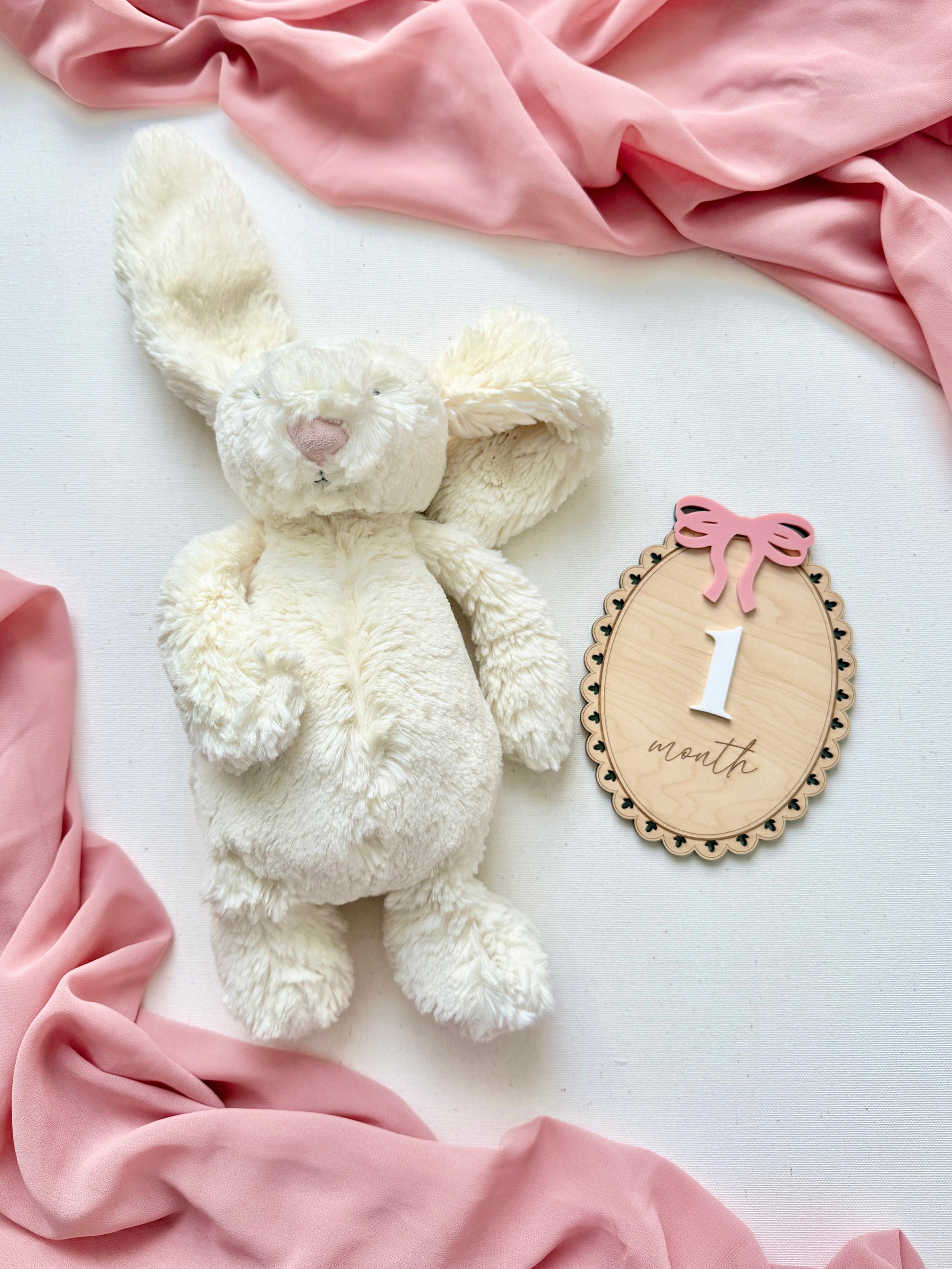 White teddy bear with a '1 month' milestone card on a pink blanket