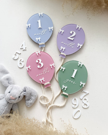Baby milestone balloon set with numbers on a soft surface with a plush toy.