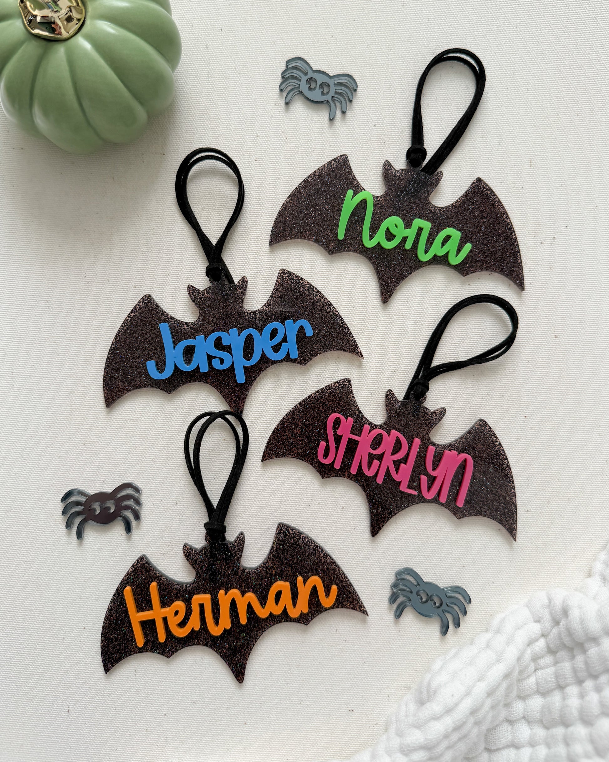 Bat-shaped keychains with personalized names on a white surface with decorative elements.