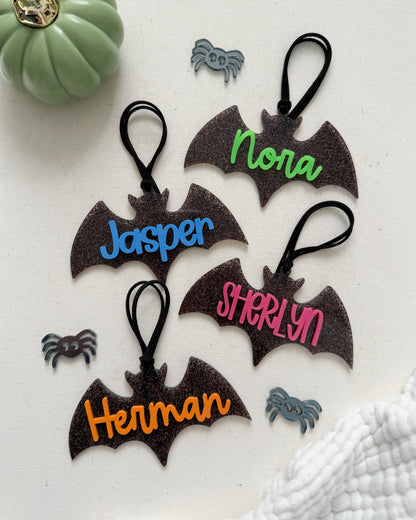 Bat-shaped keychains with personalized names on a white surface with decorative elements.