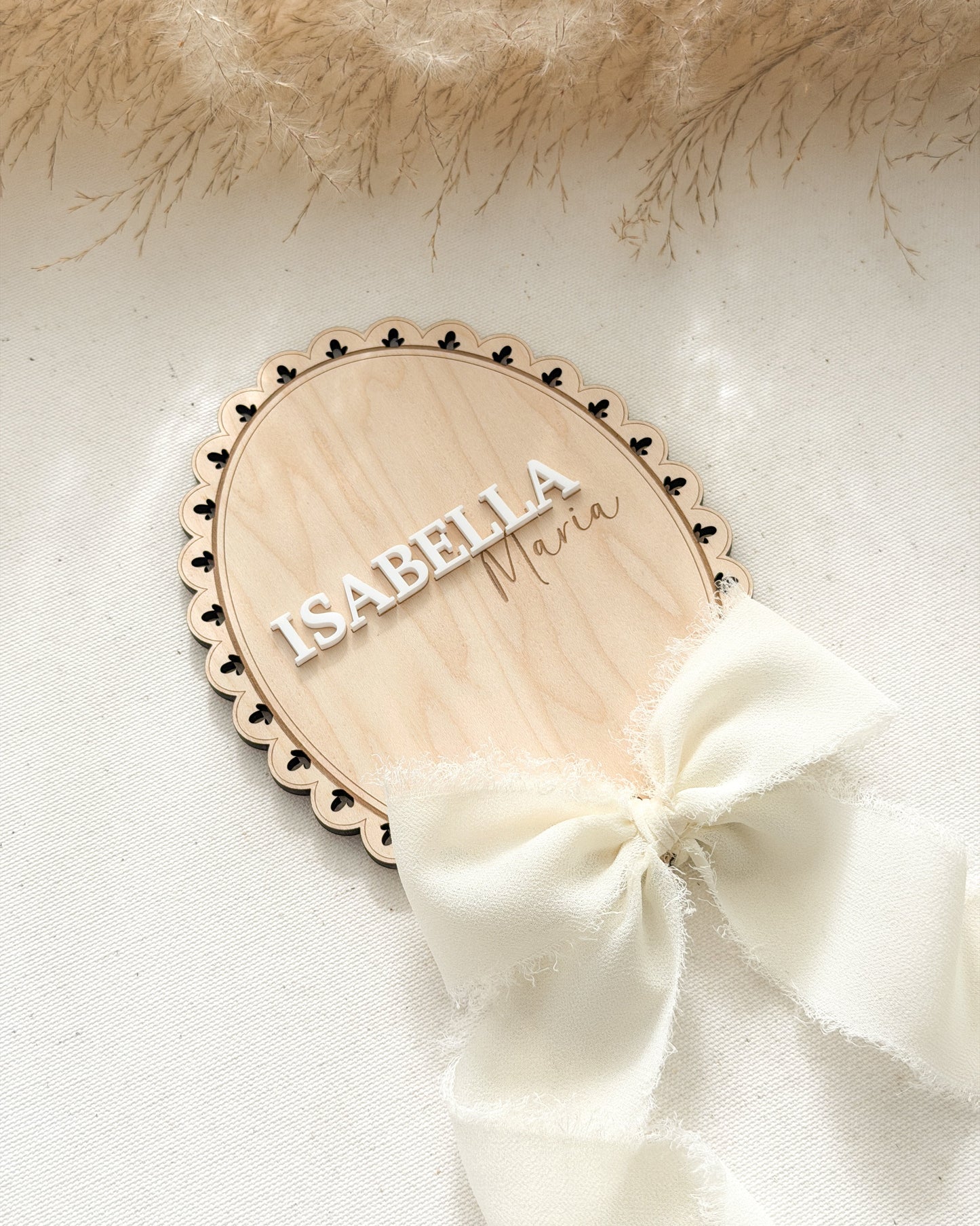 Wooden name plaque with 'Isabella' on a white background with a white bow and beige fur.