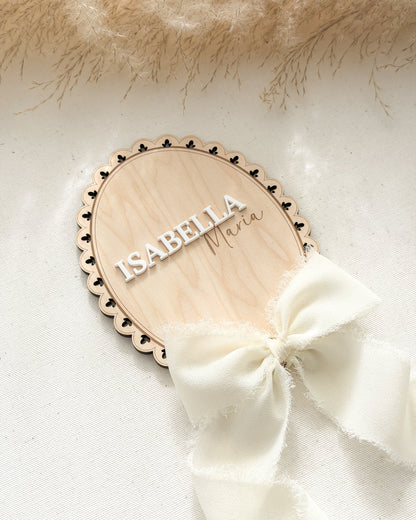 Wooden name plaque with 'Isabella' on a white background with a white bow and beige fur.