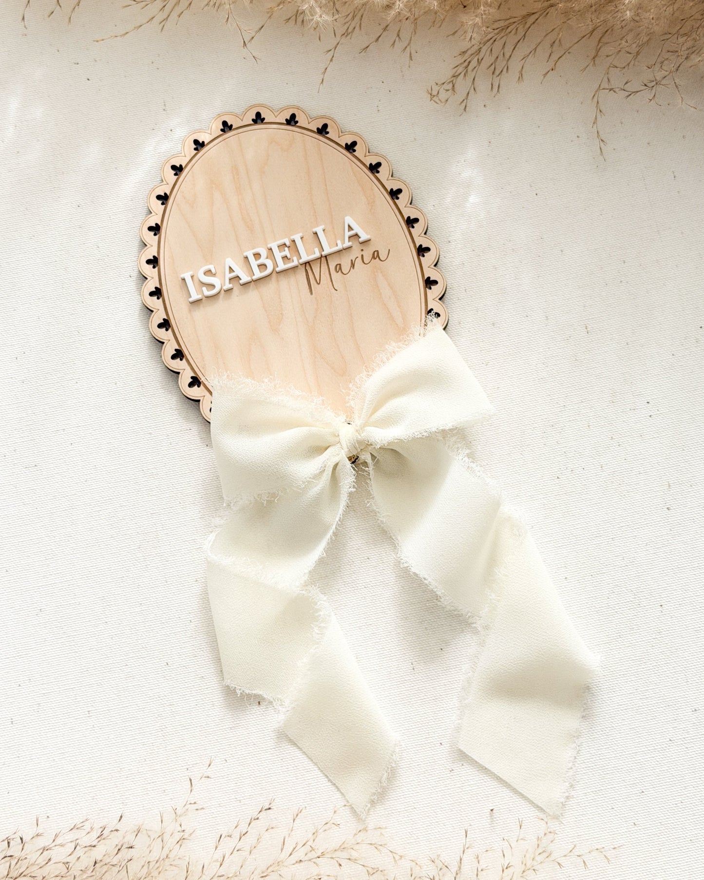 Wooden nameplate with 'Isabella' and a white bow on a textured surface