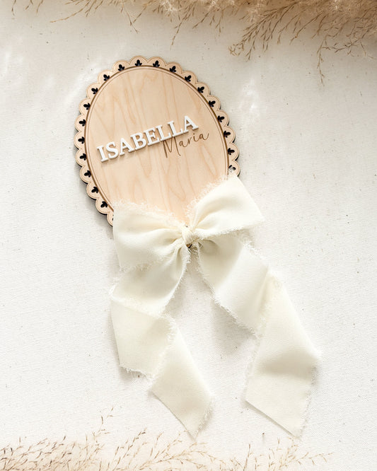 Wooden nameplate with 'Isabella' and a white bow on a textured surface