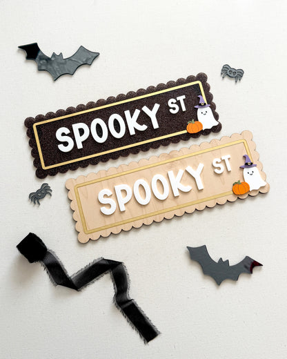 Two Halloween-themed decorative sign pieces reading “SPOOKY ST” on a white background, surrounded by small bat, spider, ghost, and pumpkin cutouts. One sign is dark brown with gold trim and white lettering, and the other is light beige with gold trim and white lettering.