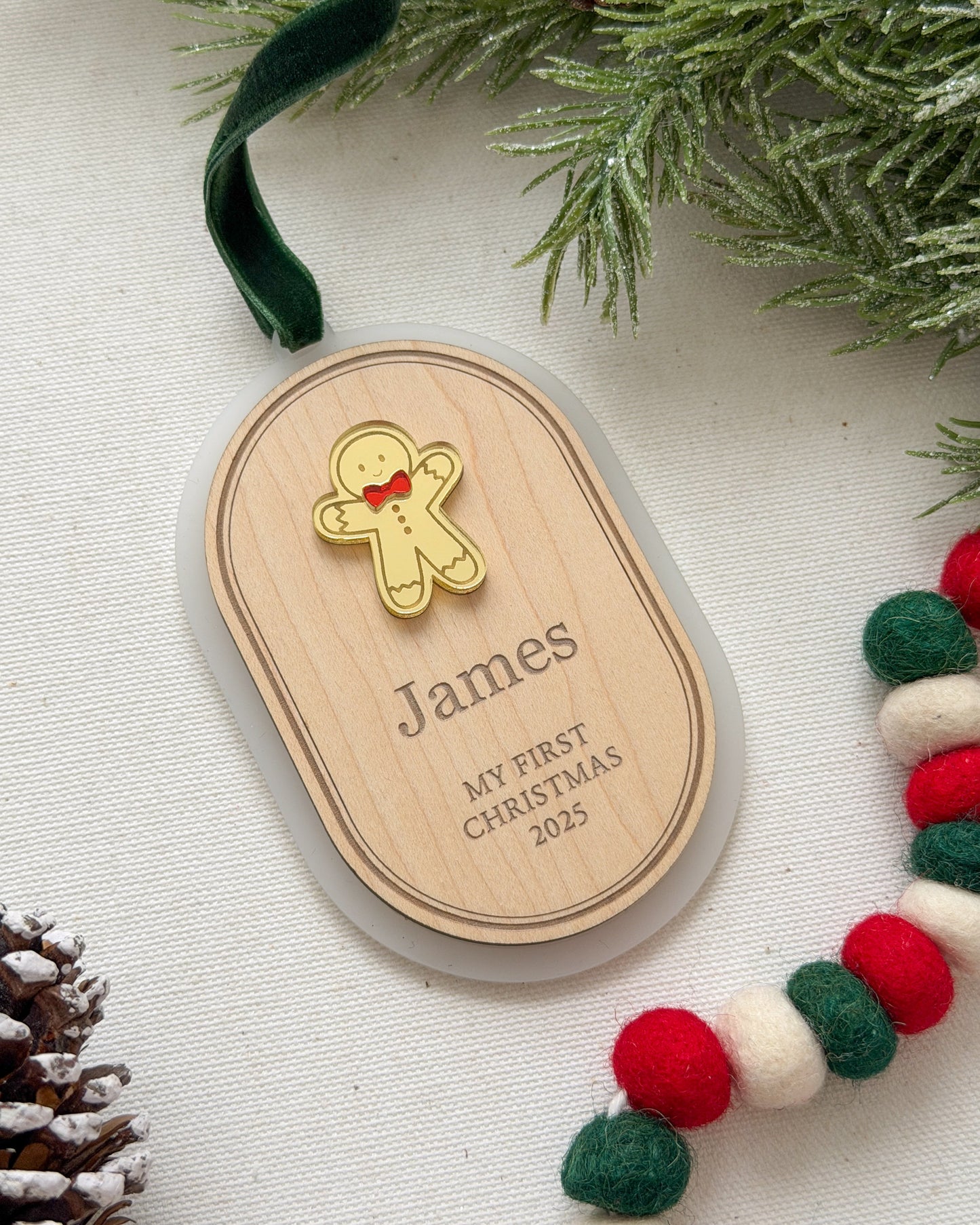 Wooden ornament with a gingerbread man design and engraved text, placed on a festive background with greenery and a ribbon.