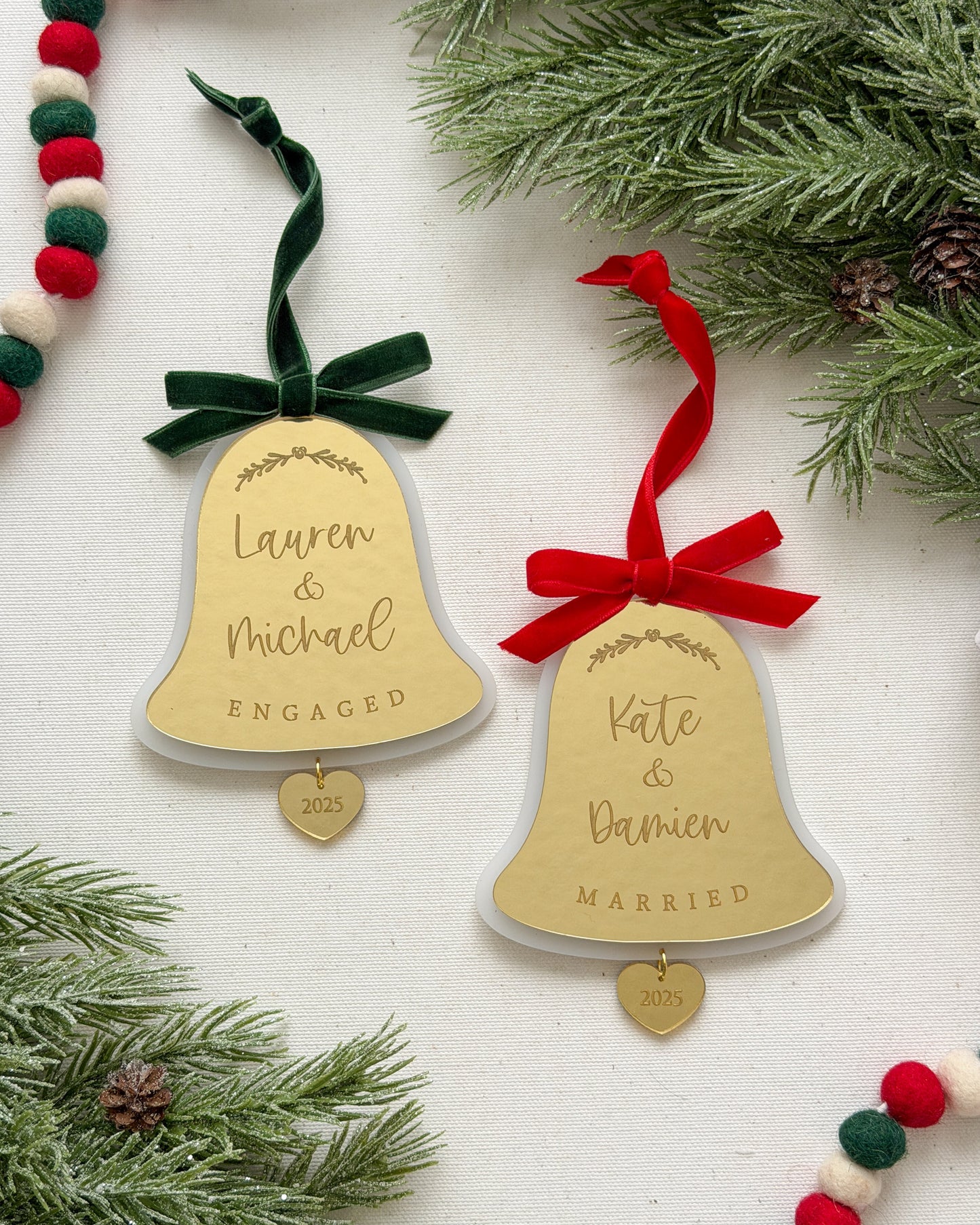 Two gold bell ornaments with names and dates on a white background with Christmas decorations.