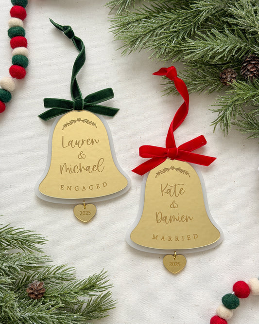 Two gold bell ornaments with names and dates on a white background with Christmas decorations.