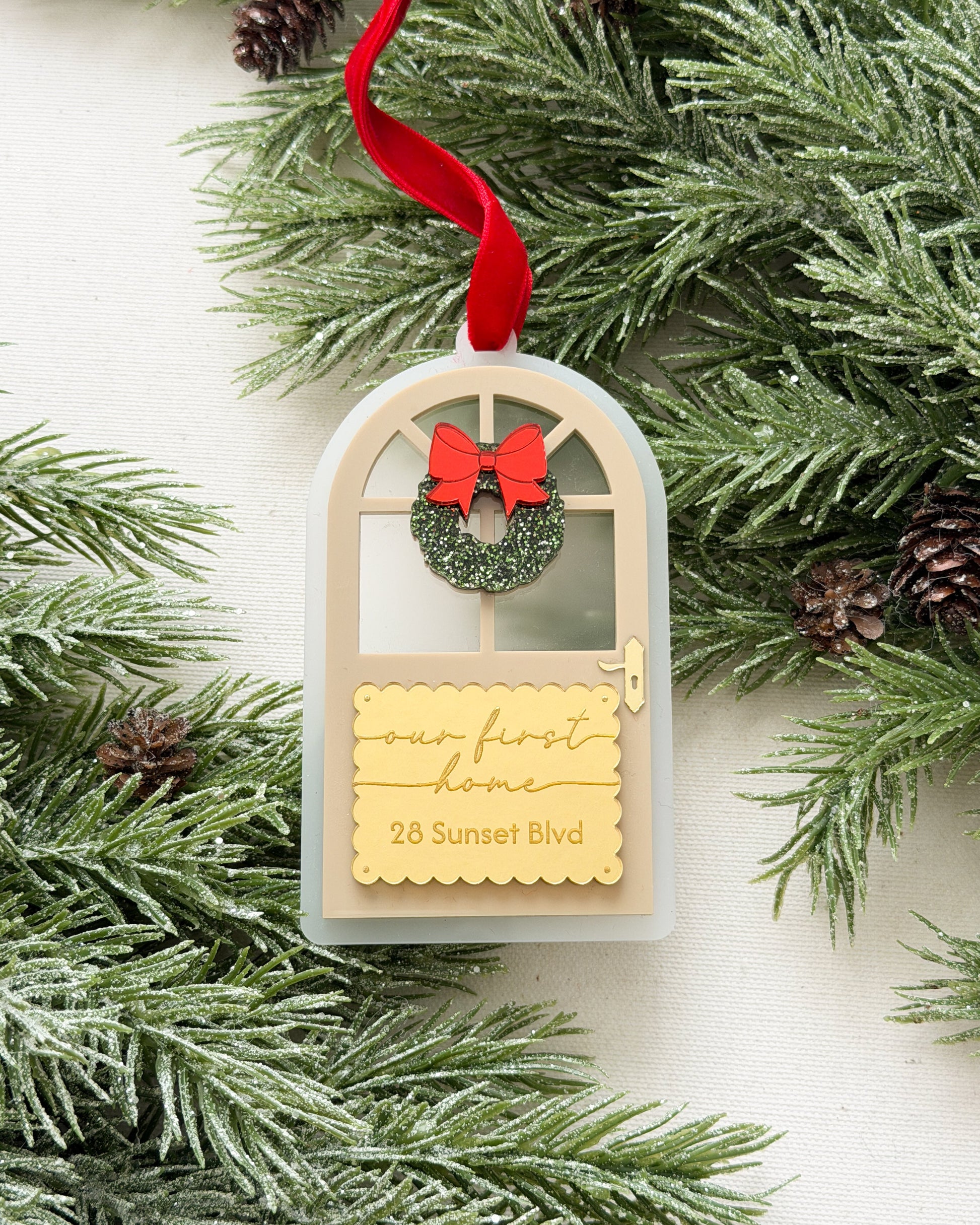 Decorative ornament with a wreath and text on a branch with pine cones