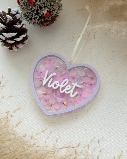 Heart-shaped decorative item with 'Violet' text on a light background with pinecones.