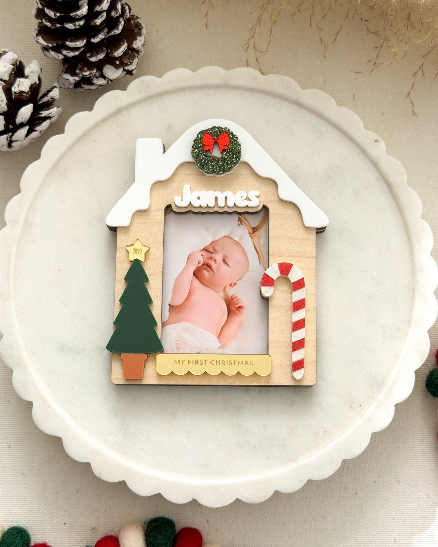 Decorative photo frame shaped like a gingerbread house with a baby photo inside, surrounded by Christmas decorations.