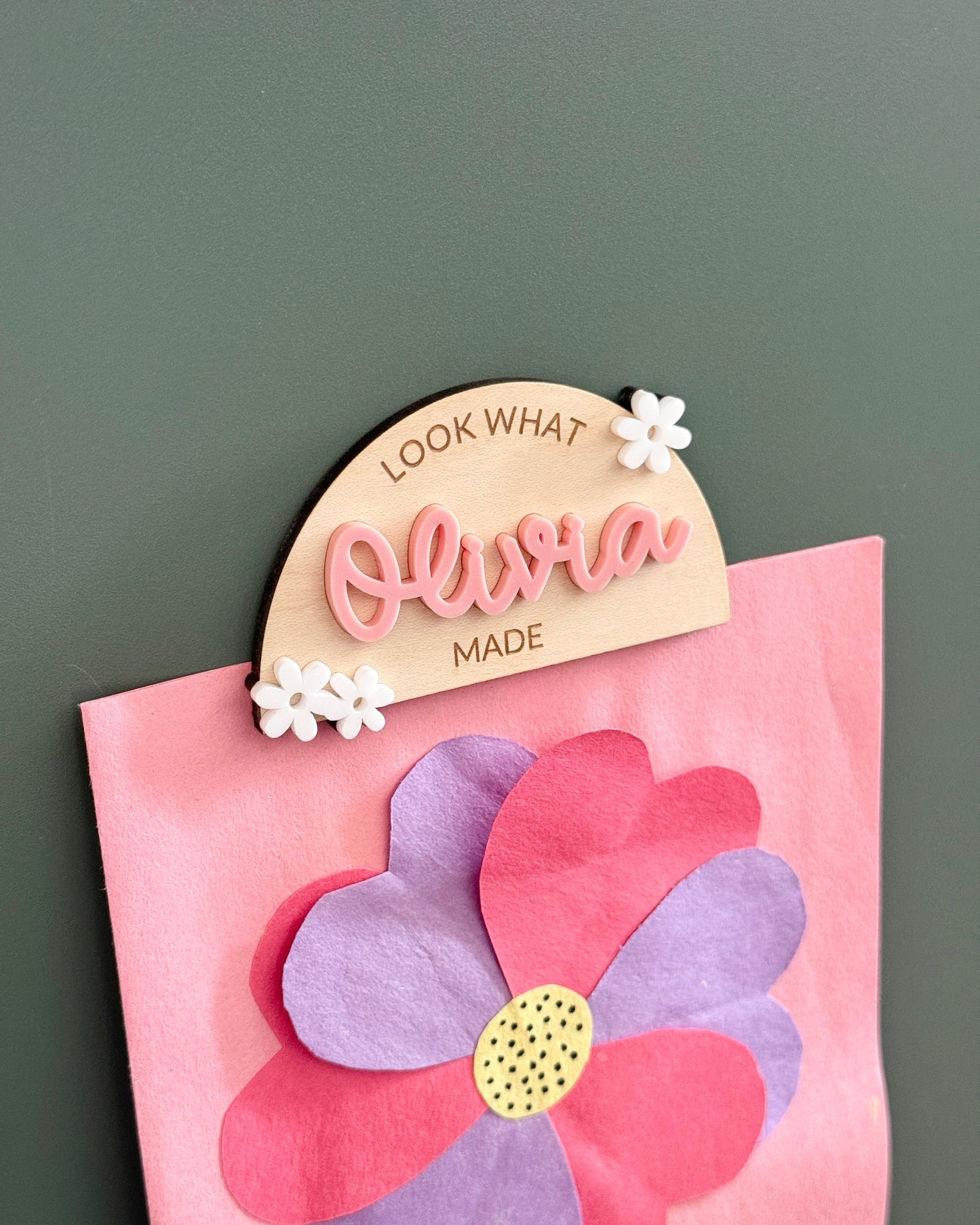 Decorative name tag with 'Olivia' on a pink flower-shaped card against a dark background