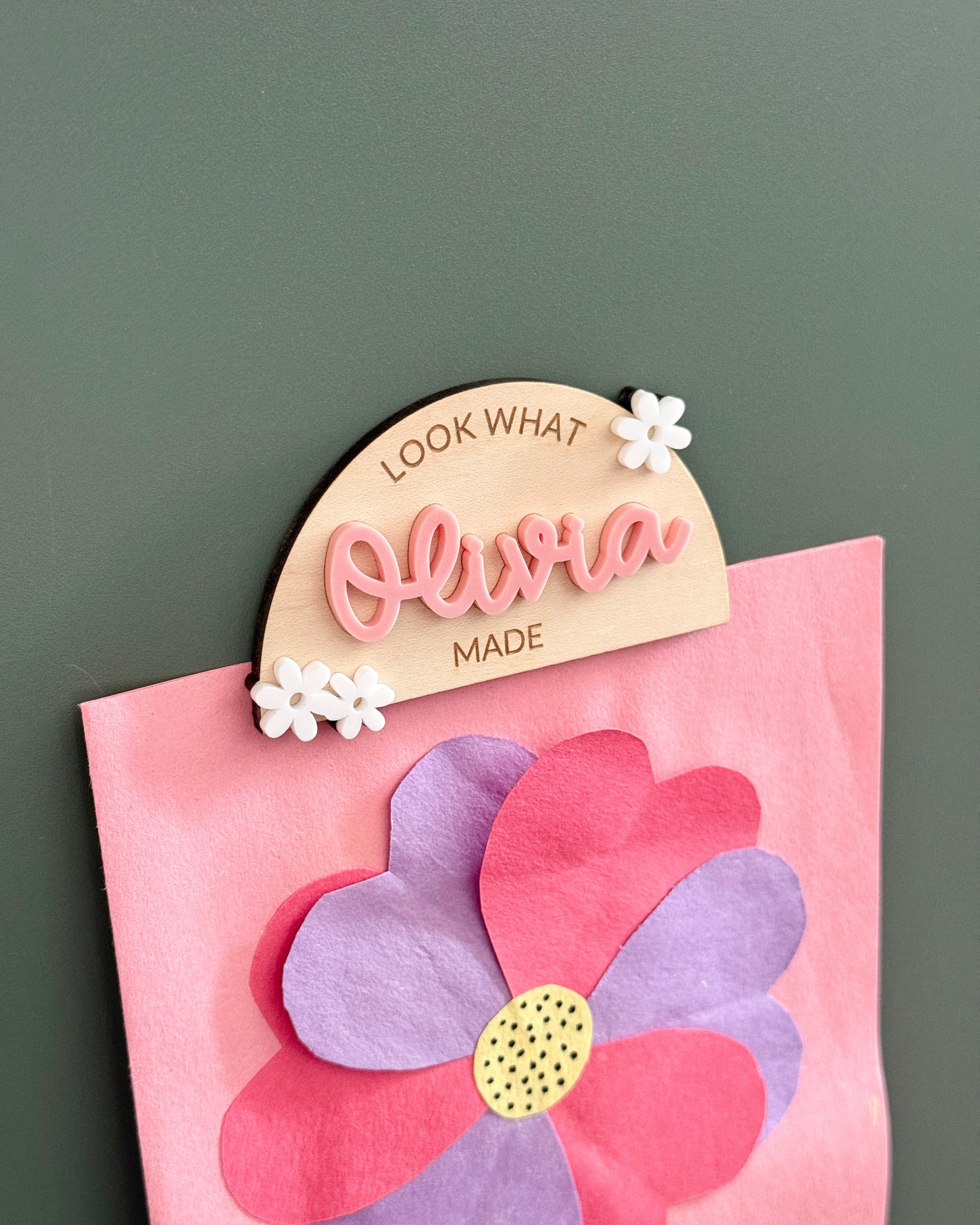 Decorative name tag with 'Olivia' on a pink flower-shaped card against a dark background