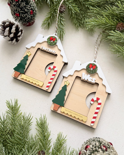 Two wooden Christmas ornaments shaped like houses with decorative elements on a white background with pine branches.