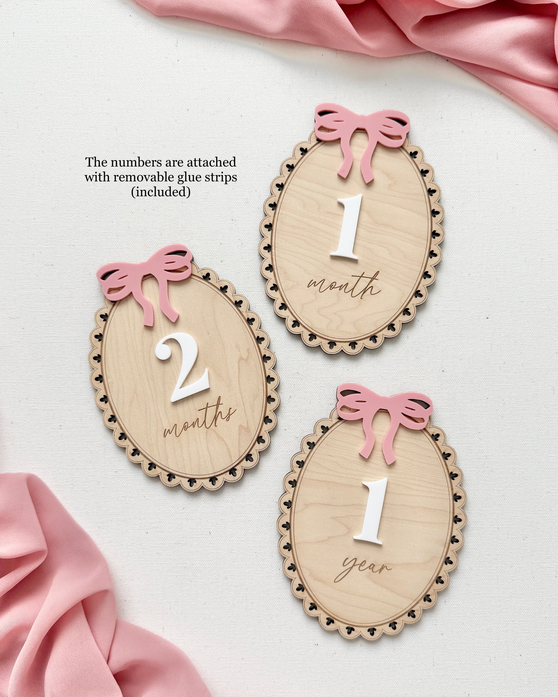 Baby milestone markers with numbers and pink ribbons on a pink fabric background