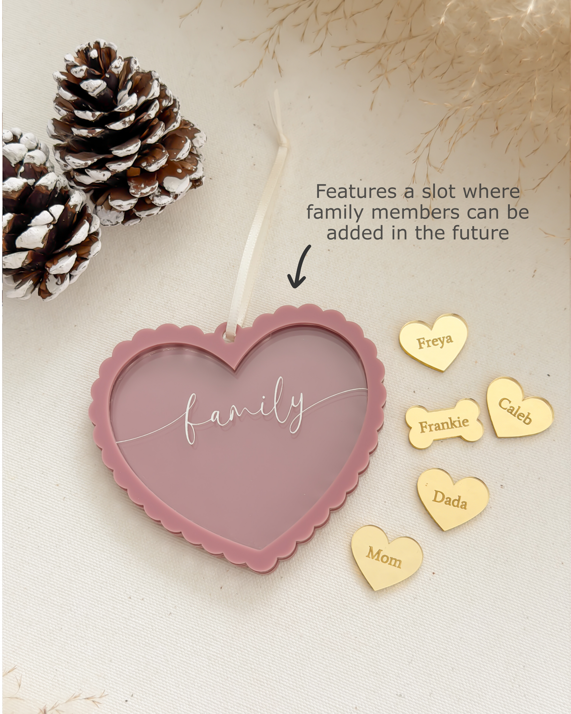 Heart-shaped pink plaque with 'family' engraving, gold heart-shaped name tags, and pinecones on a light background.